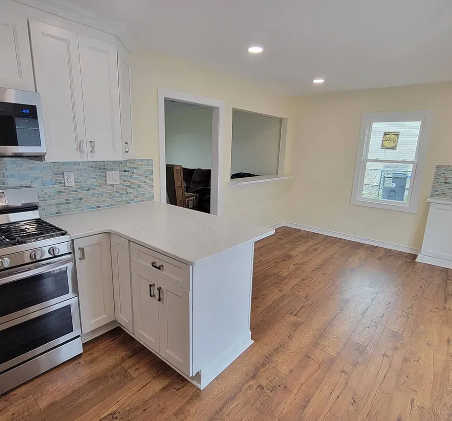 Bright white kitchen with stainless stove, island counter, and hardwood floor leading to a sunlit dining area