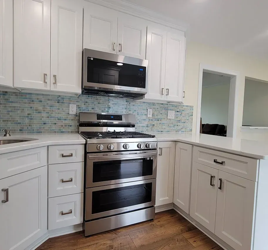 Bright white kitchen with stainless steel stove and microwave, light blue tile backsplash, and wood floor
