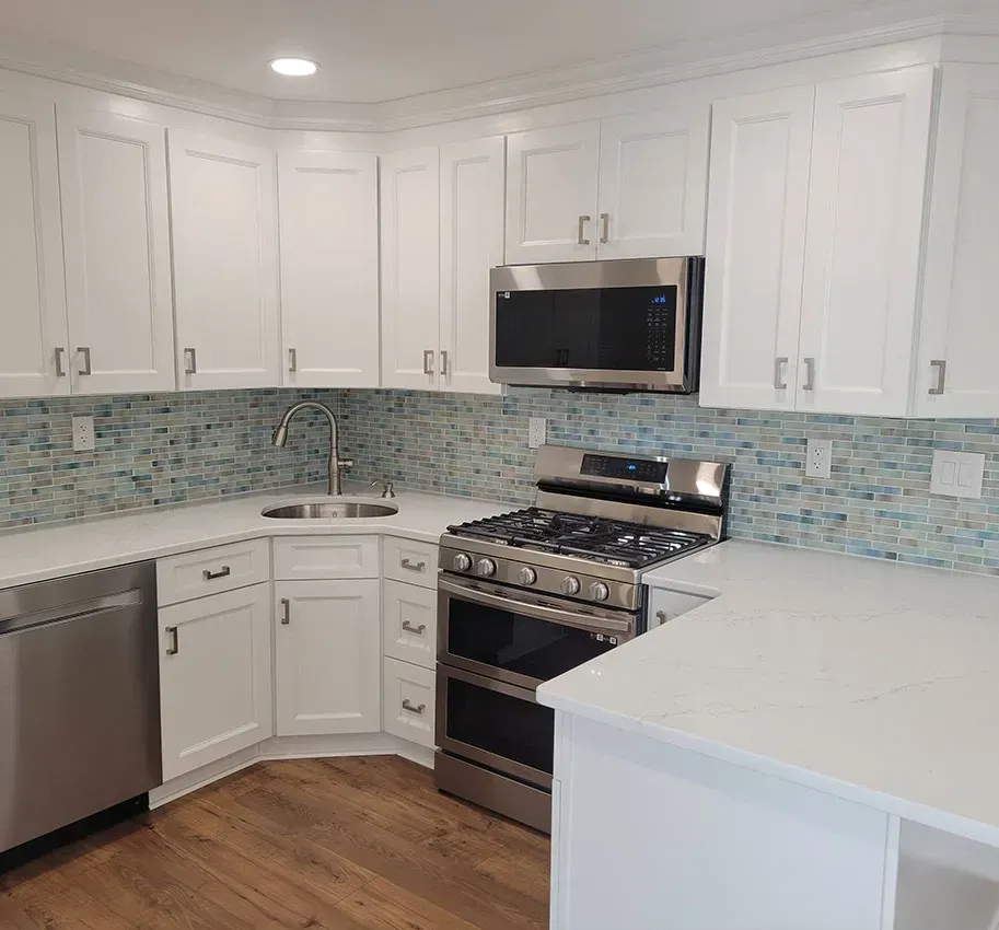 Bright white kitchen with stainless steel appliances, light blue tile backsplash, and wood floor.