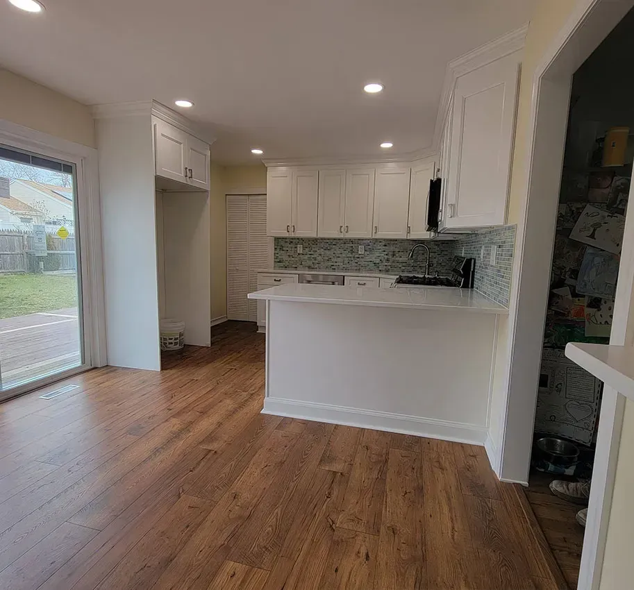 Empty modern kitchen and dining area with white cabinets, wood floors, and a sliding glass door