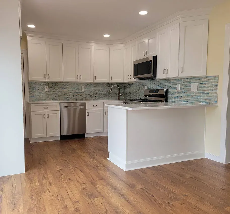 Bright modern white kitchen with wood floors, stainless appliances, and a blue tile backsplash