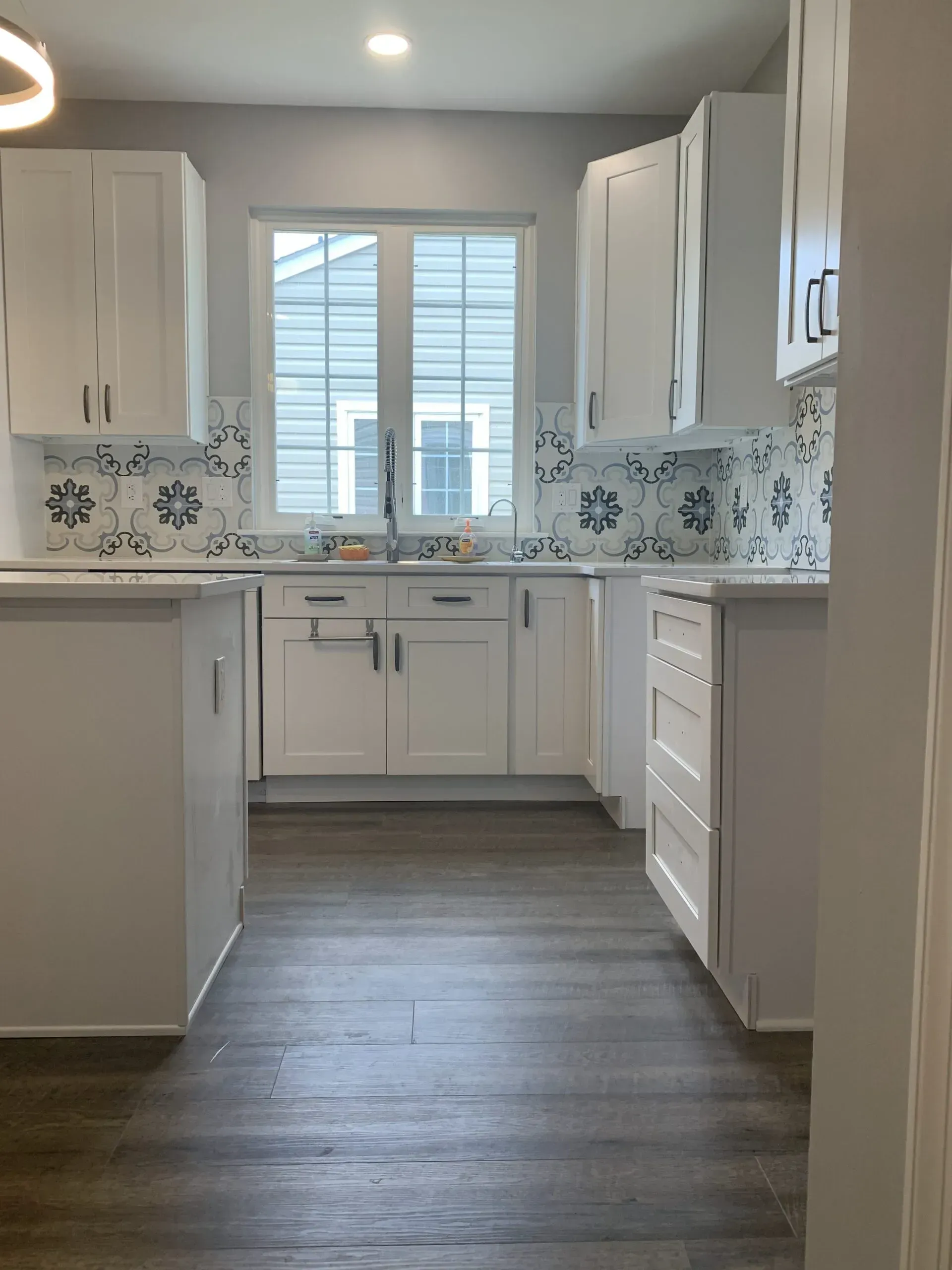 Bright modern kitchen with white cabinets, gray flooring, and a window over the sink