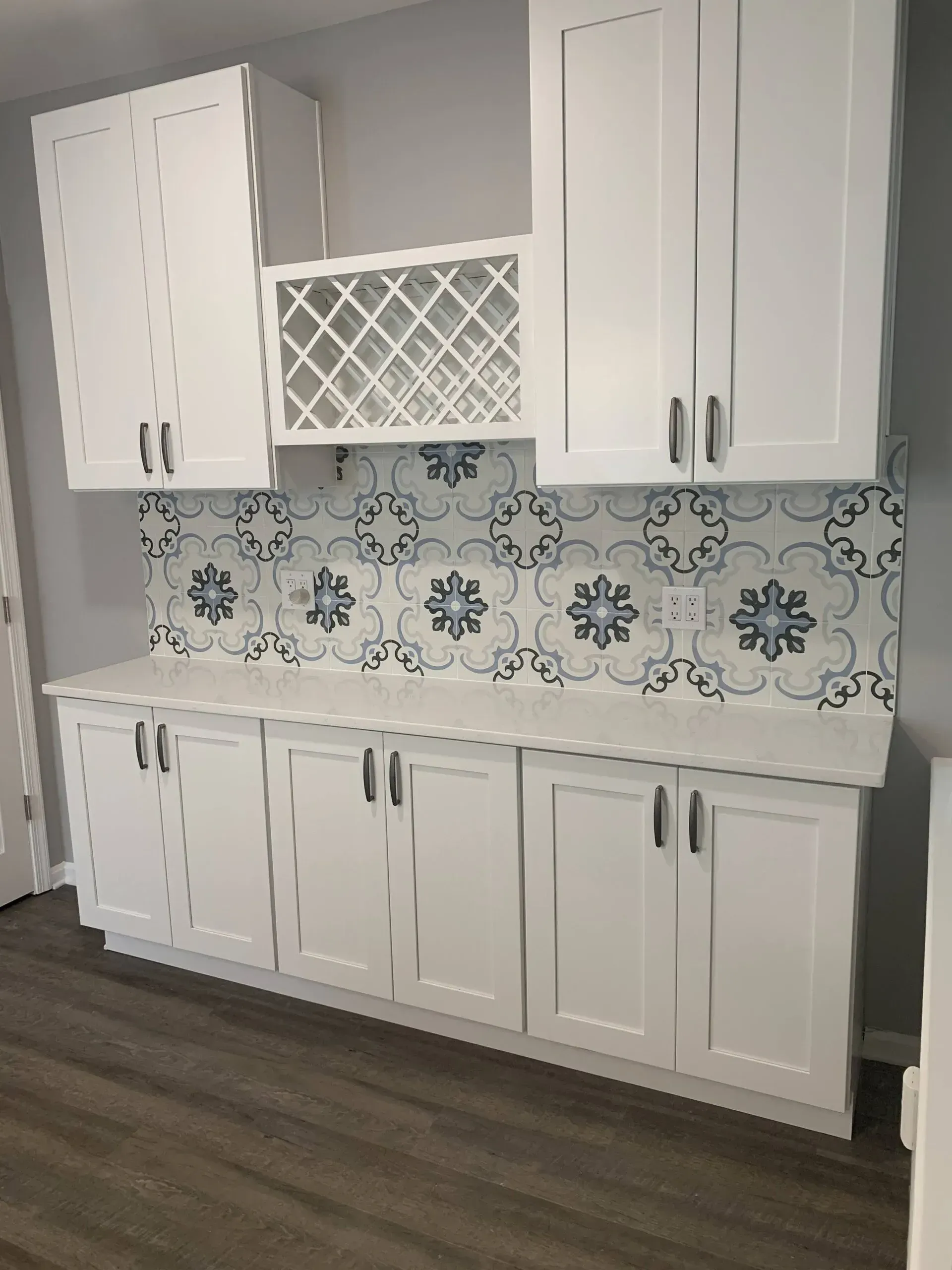 White kitchen cabinets with blue patterned tile backsplash and wood flooring.