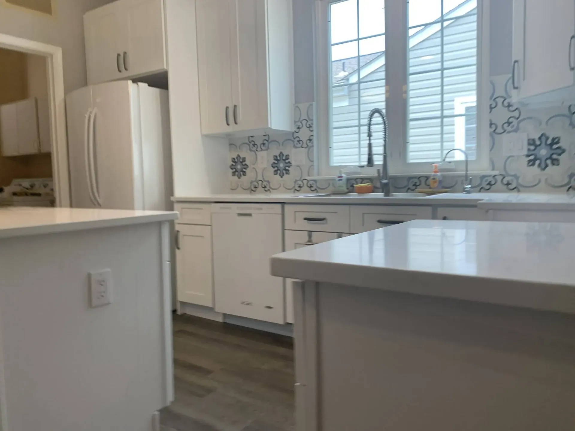Bright white kitchen with island, cabinets, fridge, window, and blue floral tile accents