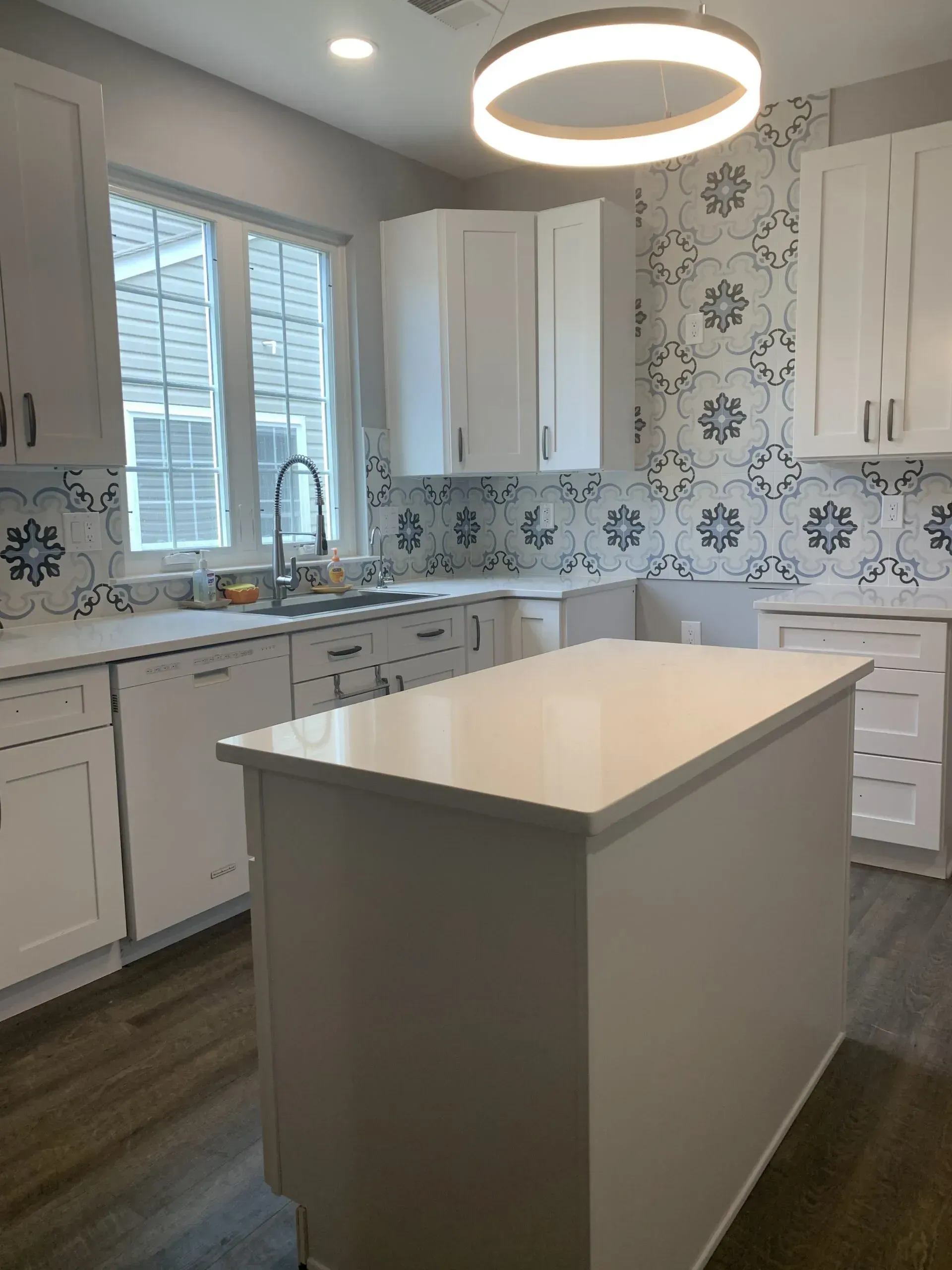 Bright modern kitchen with white cabinets, patterned backsplash, and a central island under a round light fixture