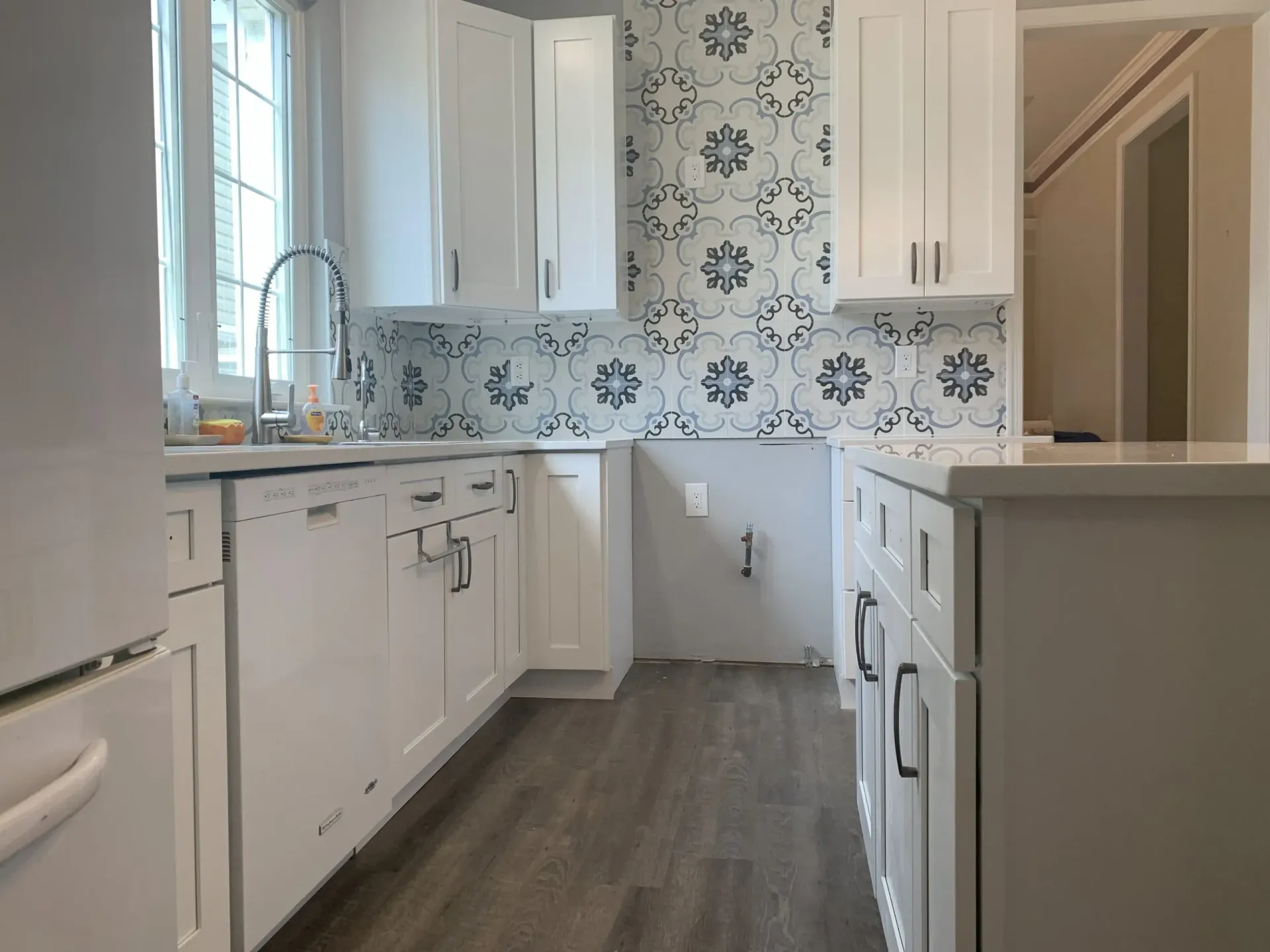 Bright white kitchen with patterned tile backsplash, gray floor, and cabinets on both sides