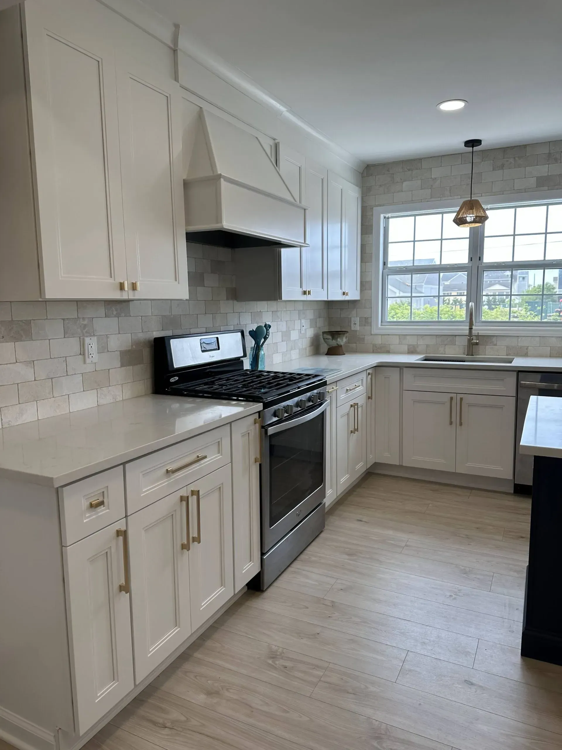 Bright white kitchen with black stove, light cabinets, tiled backsplash, and a window over the sink