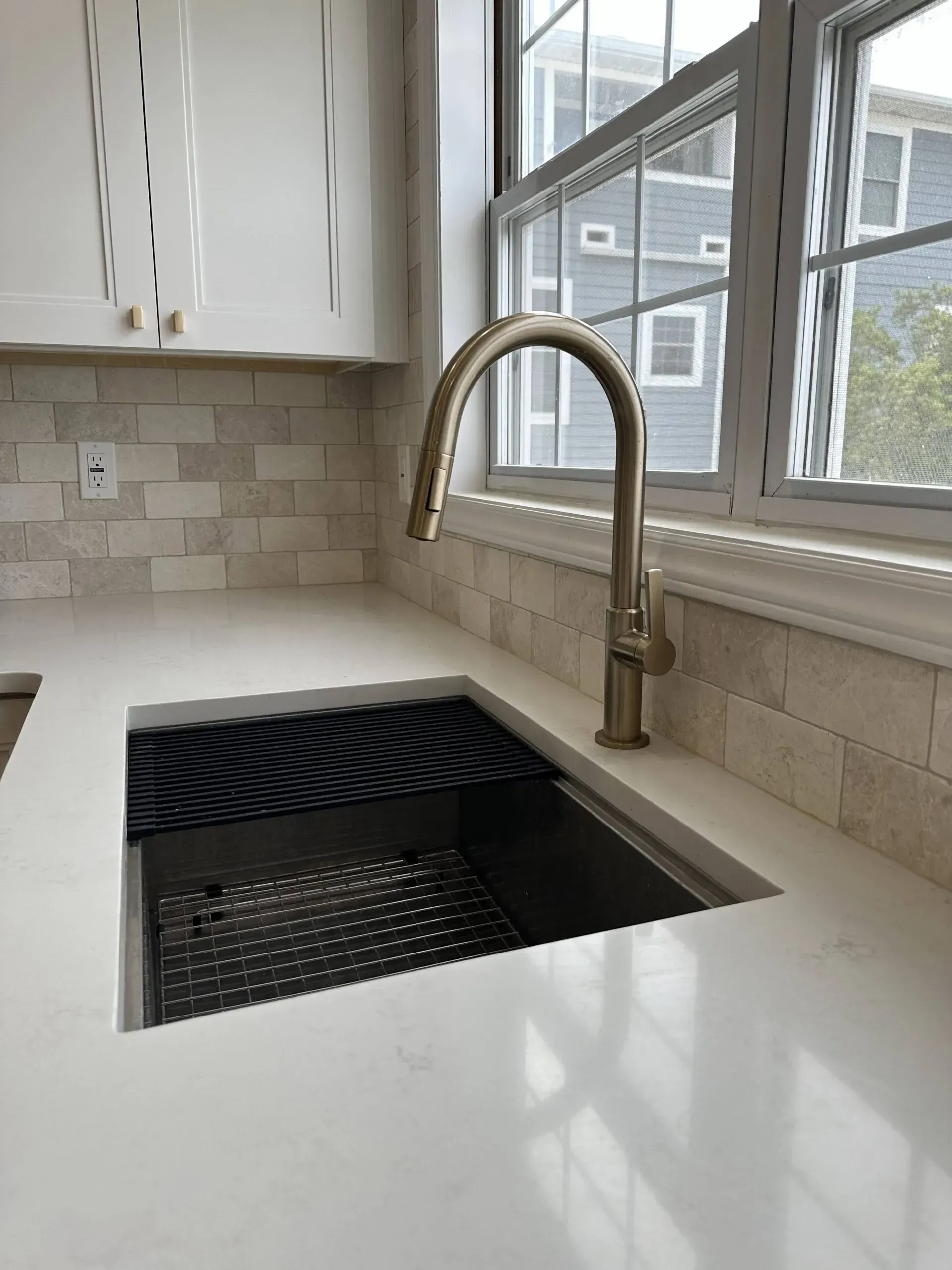 Modern kitchen sink with tall brushed-metal faucet beside a bright window and tiled backsplash