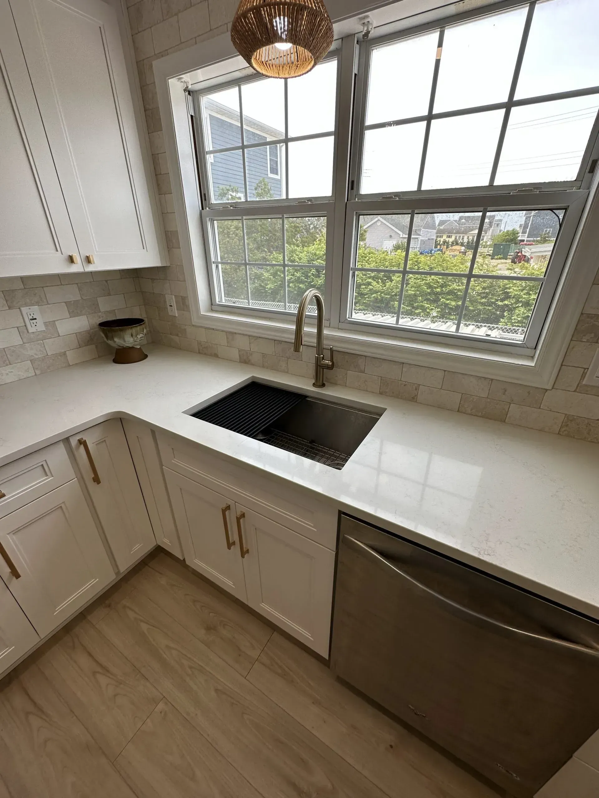 Bright white kitchen corner with sink under a window, stainless dishwasher, and light wood floor