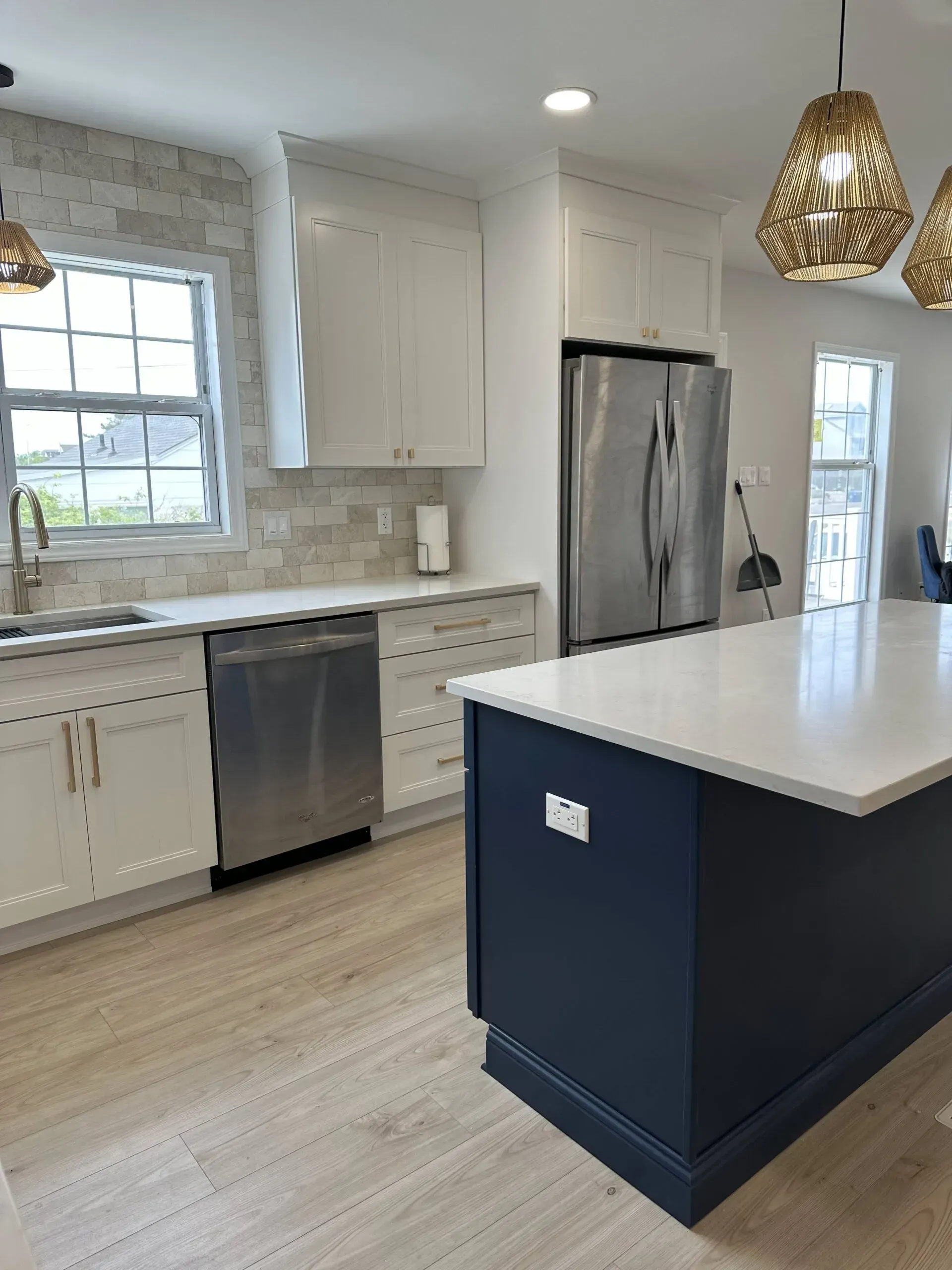 Bright modern kitchen with white cabinets, stainless appliances, and a navy island under pendant lights