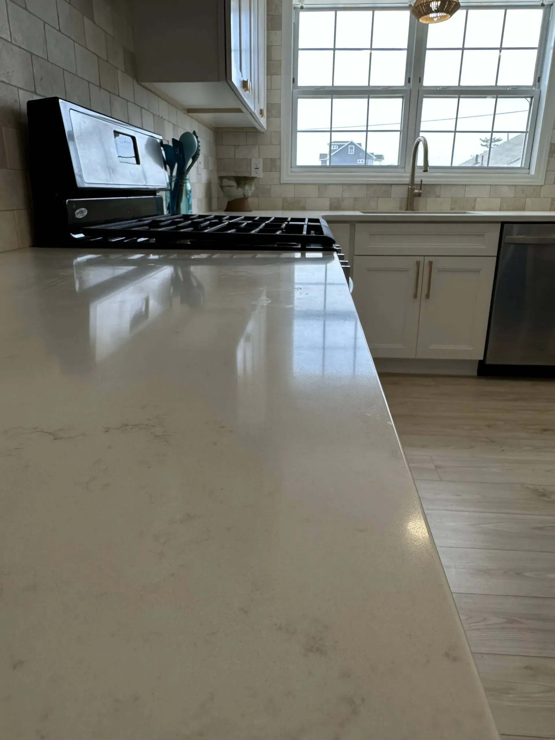 Modern kitchen with glossy white island countertop, black stove, and sunlit window over sink