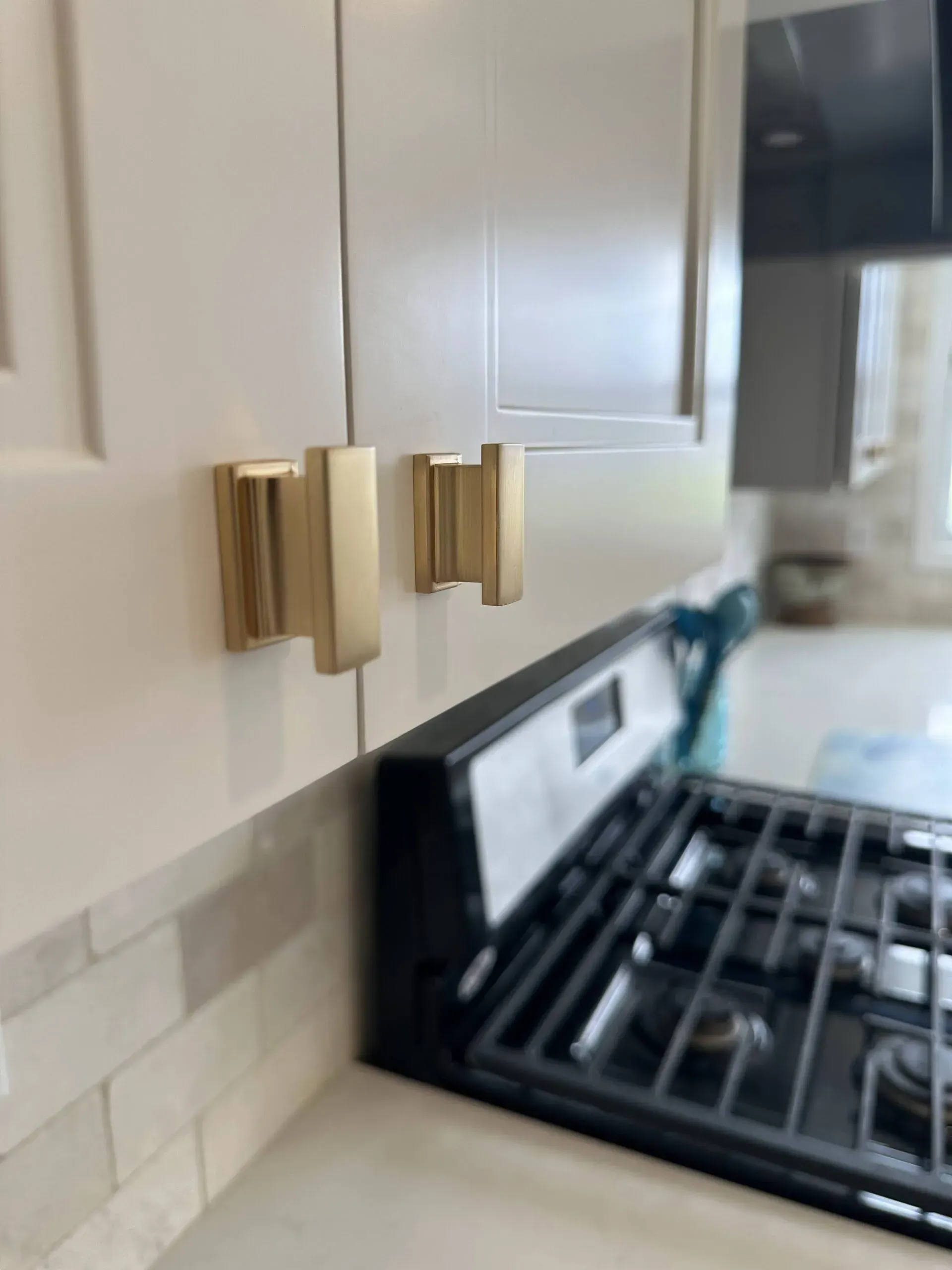 White kitchen cabinets with gold handles beside a black gas stove and light tile backsplash