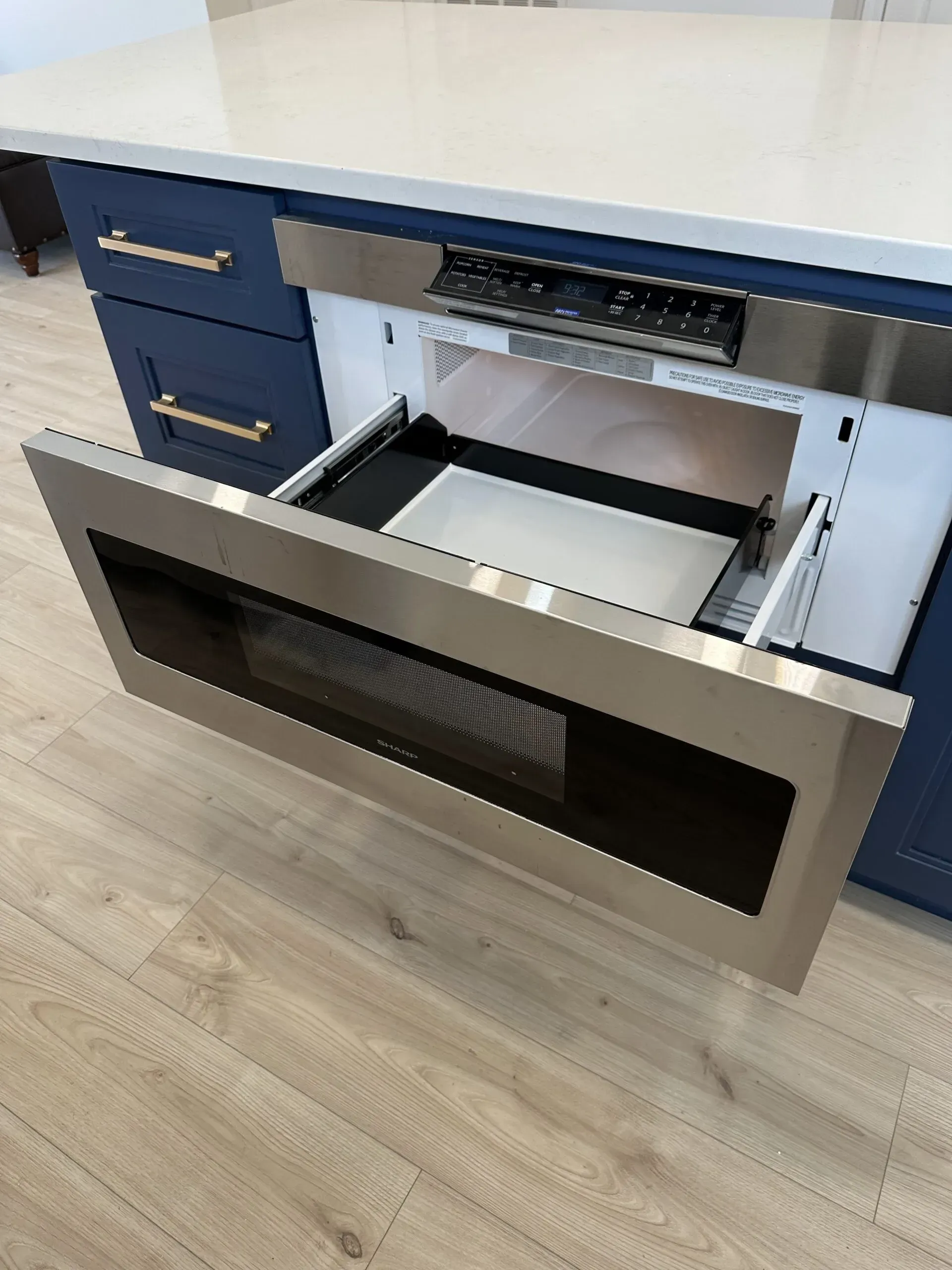 Open kitchen drawer with pull-out bin and dark blue cabinets, showing a built-in trash compartment.