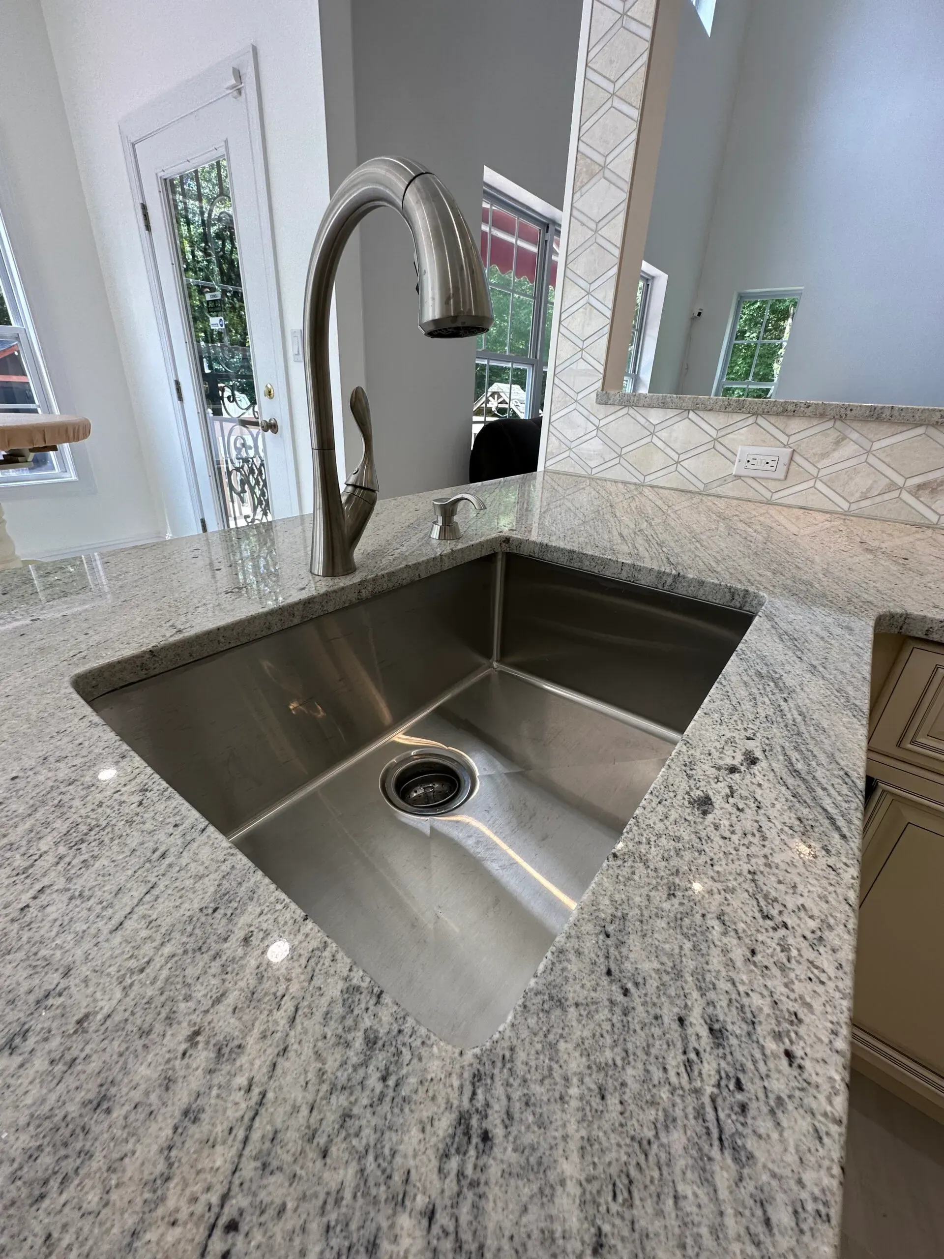 Stainless-steel kitchen sink with chrome faucet set in a speckled granite countertop.