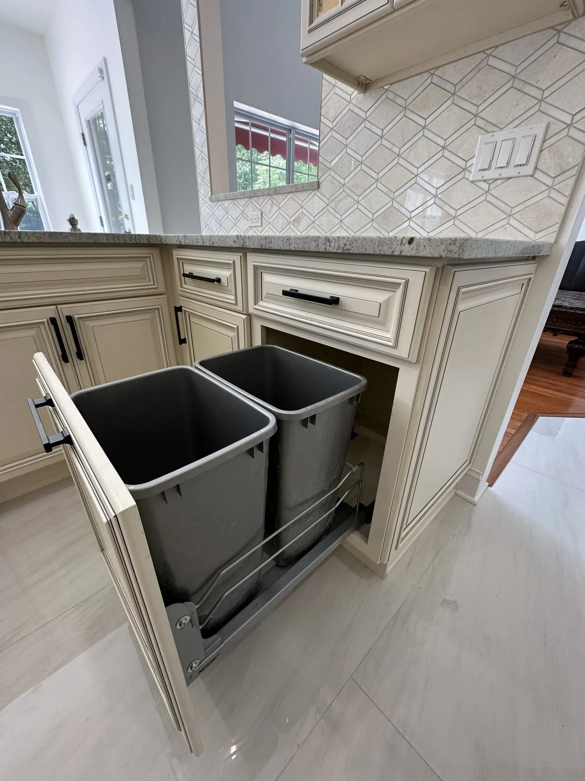 Kitchen pull-out trash cabinet with two gray bins open beside a countertop and sink
