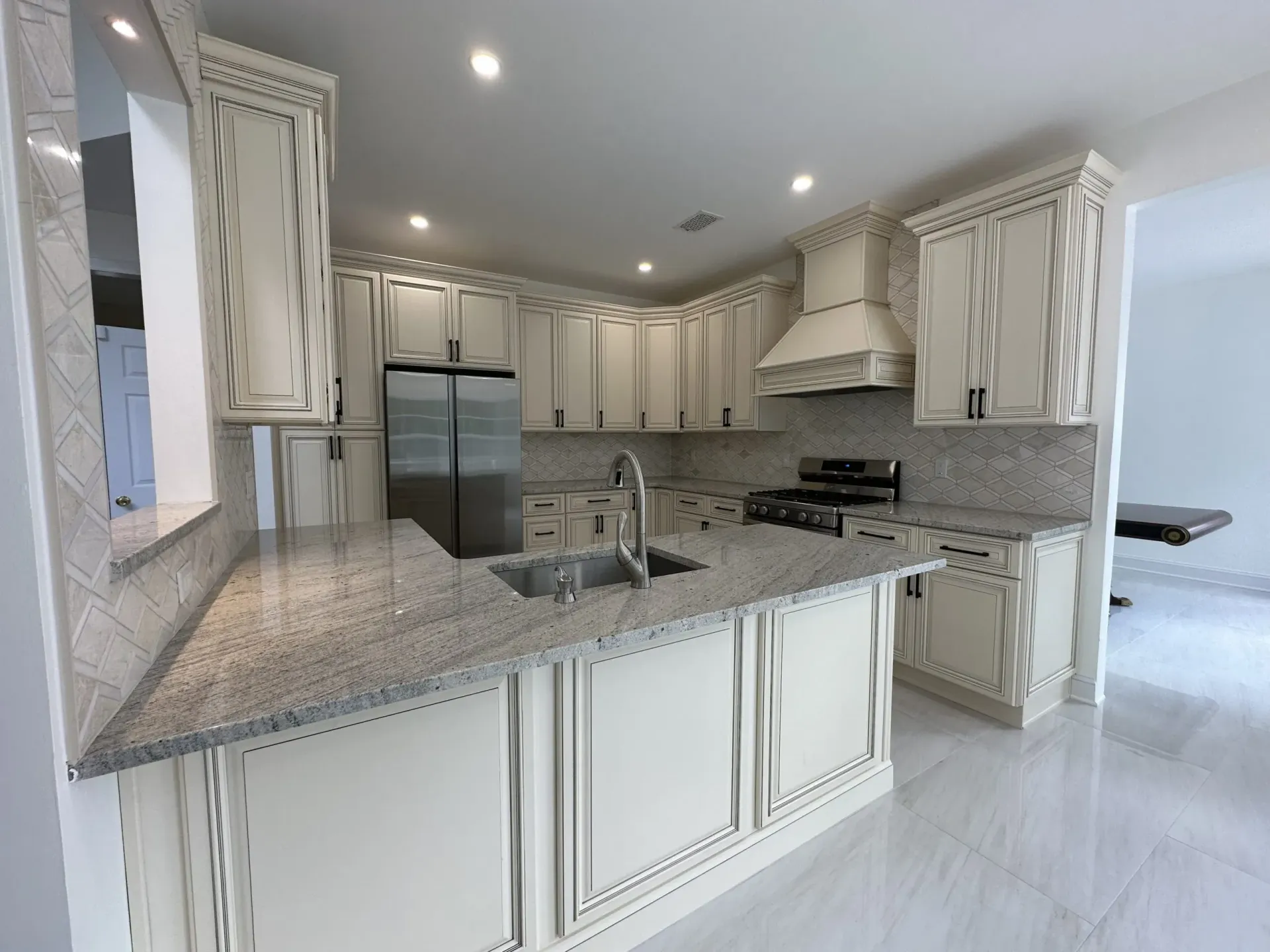 Bright white kitchen with granite island, stainless steel fridge, and ornate cabinets