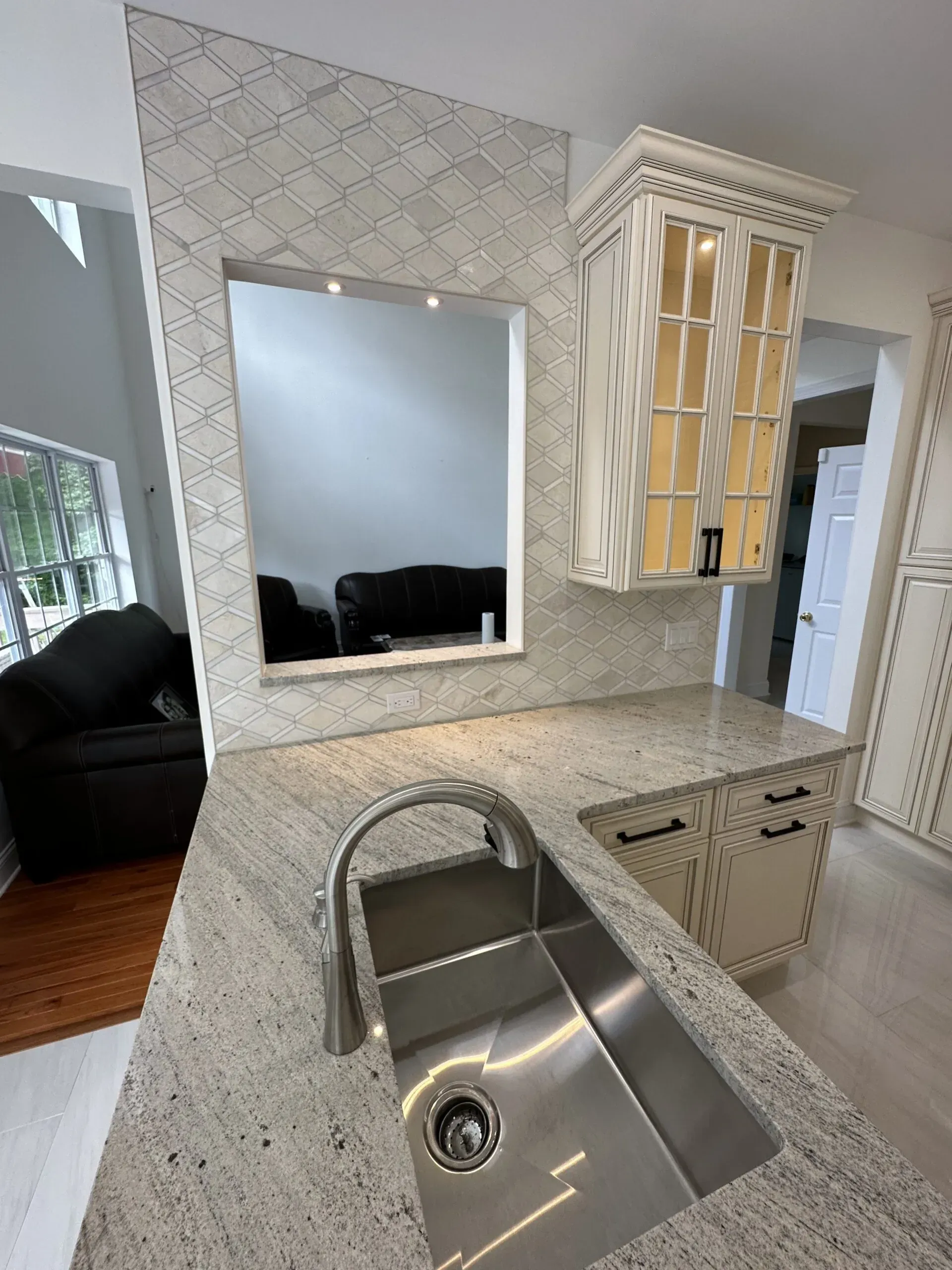 Kitchen sink and speckled countertop with mirror backsplash and hanging glass cabinet.