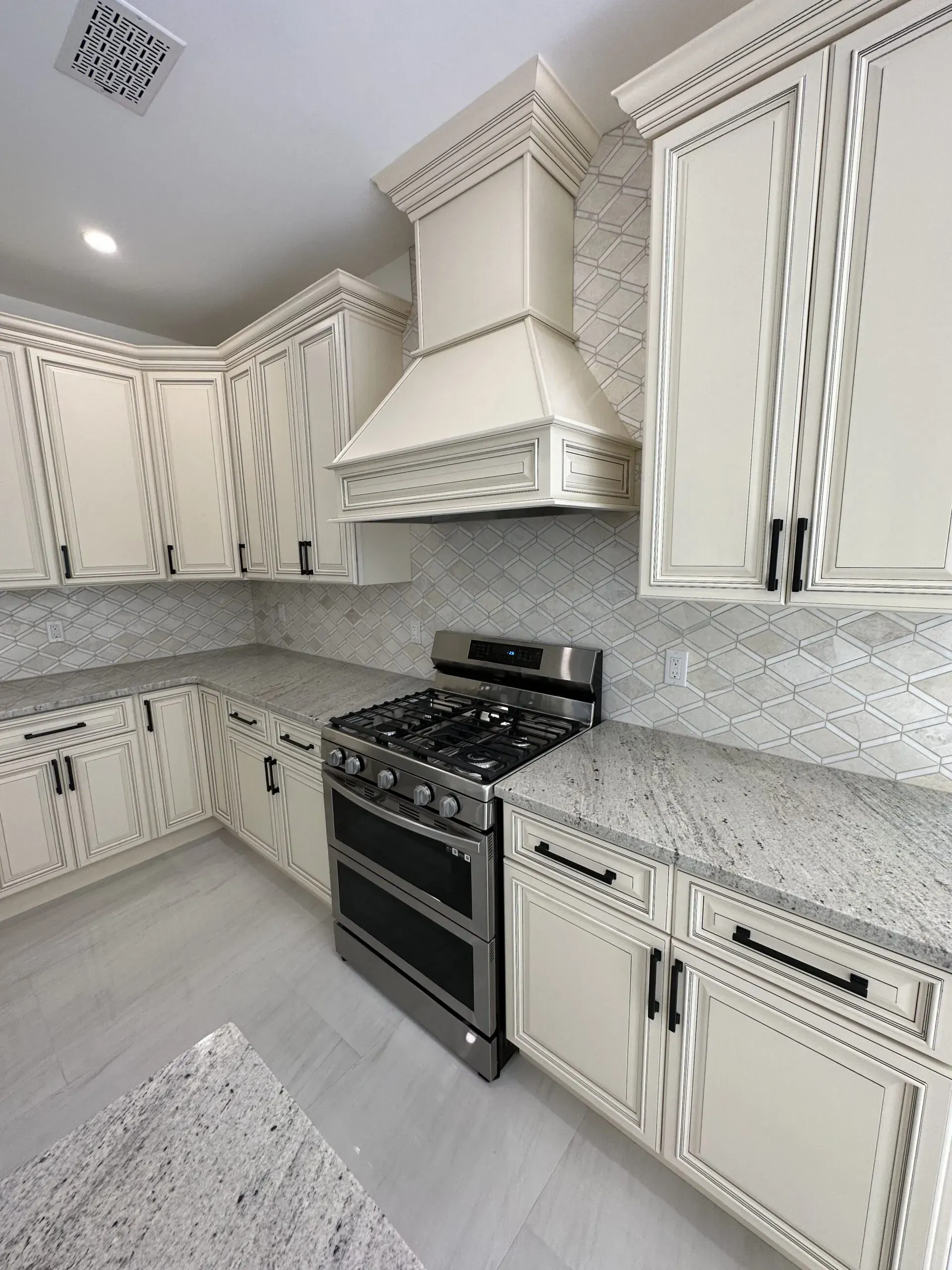Bright white kitchen with ornate cabinets, gray speckled countertops, and black stove with matching hood.