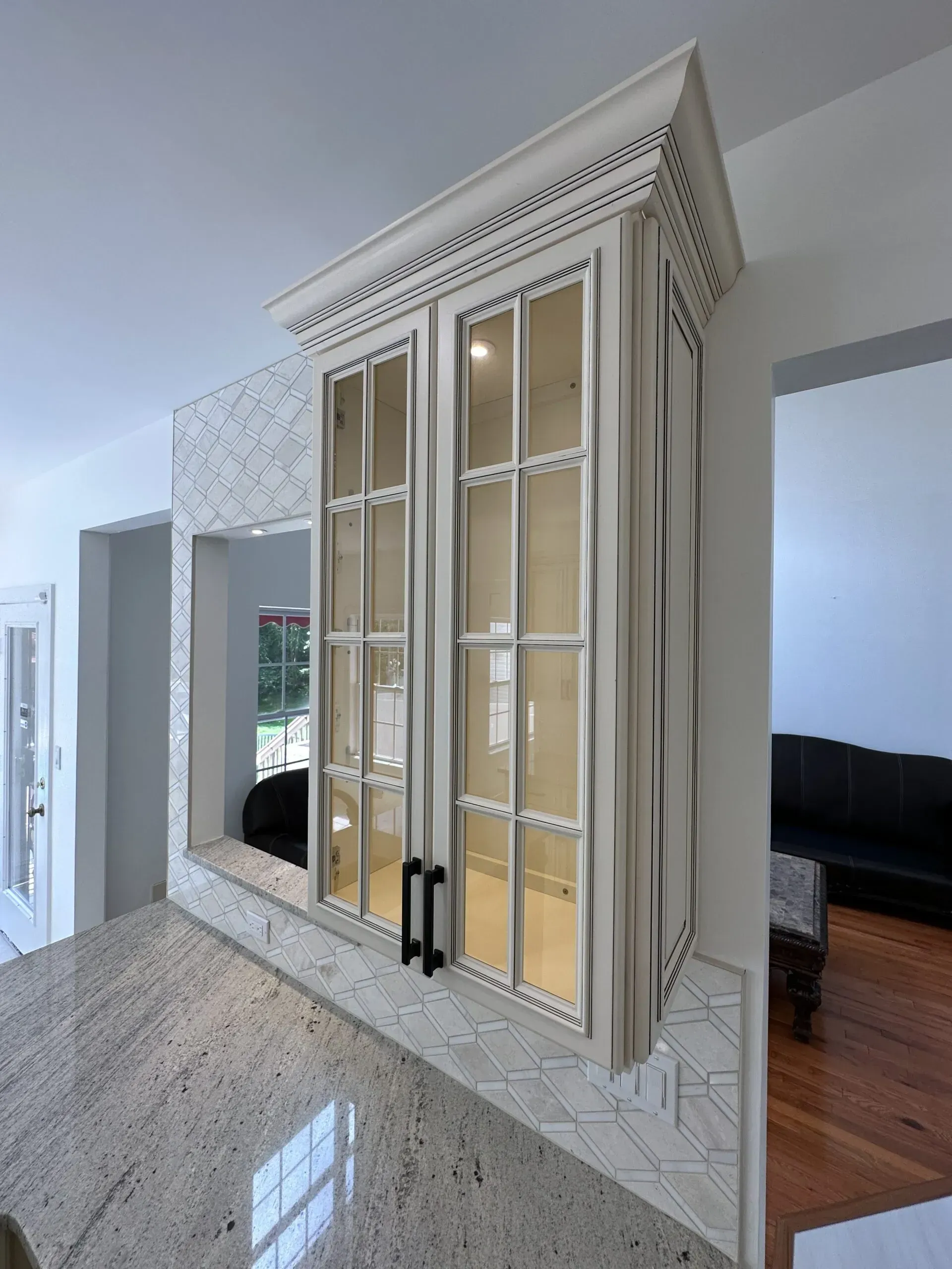 Built-in glass-front cabinet with mirrored panels in a bright hallway, beside a doorway and living room.
