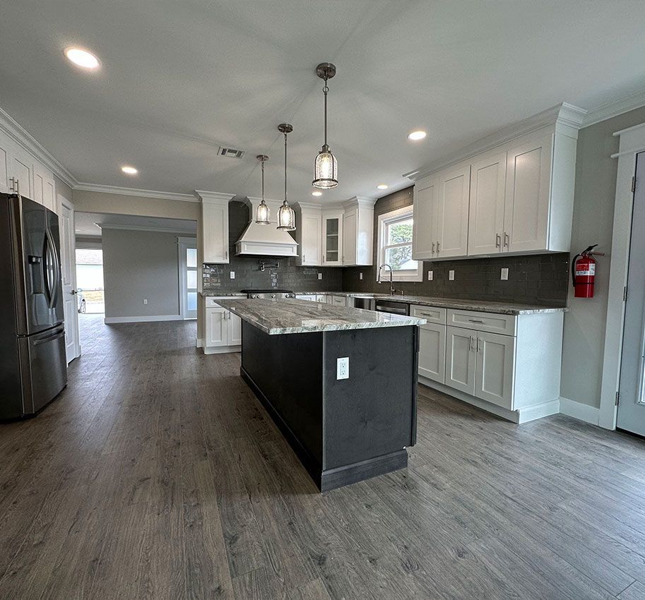 Modern kitchen with dark island, white cabinets, pendant lights, and wood-look flooring