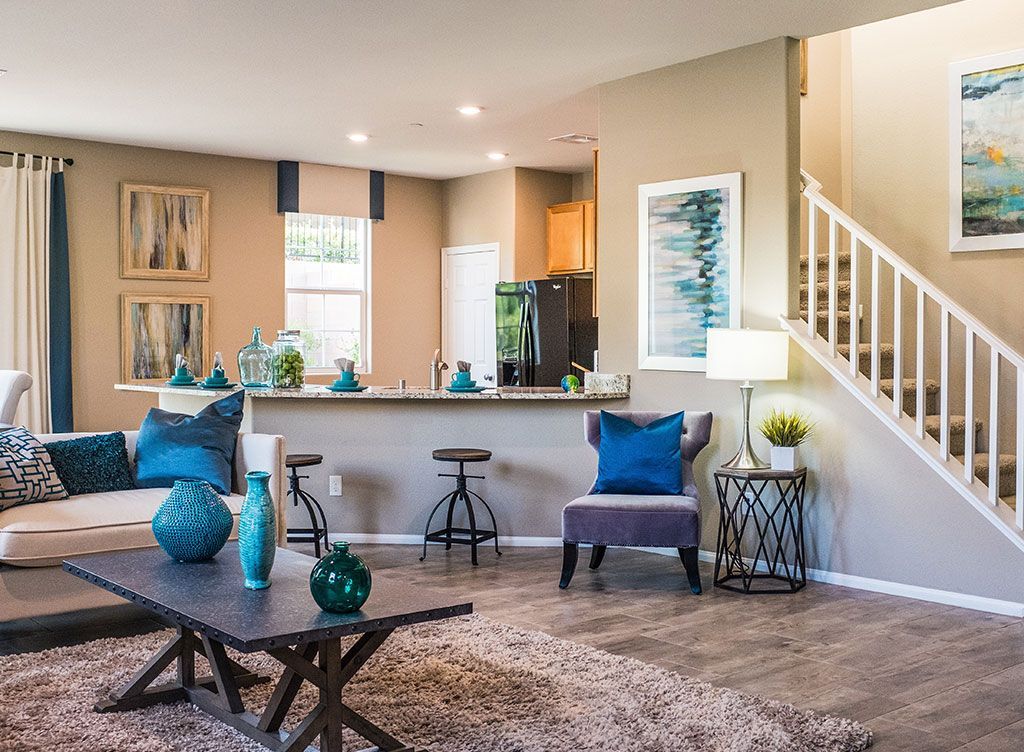 Bright living room with blue accents, a kitchen counter, staircase, and patterned rug.