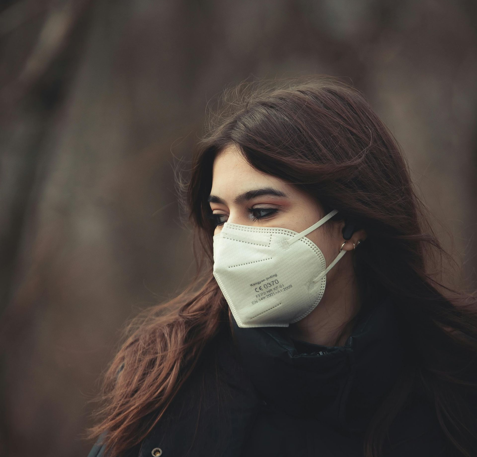 A person wearing a white KN95 respirator gazes into the distance pensively.