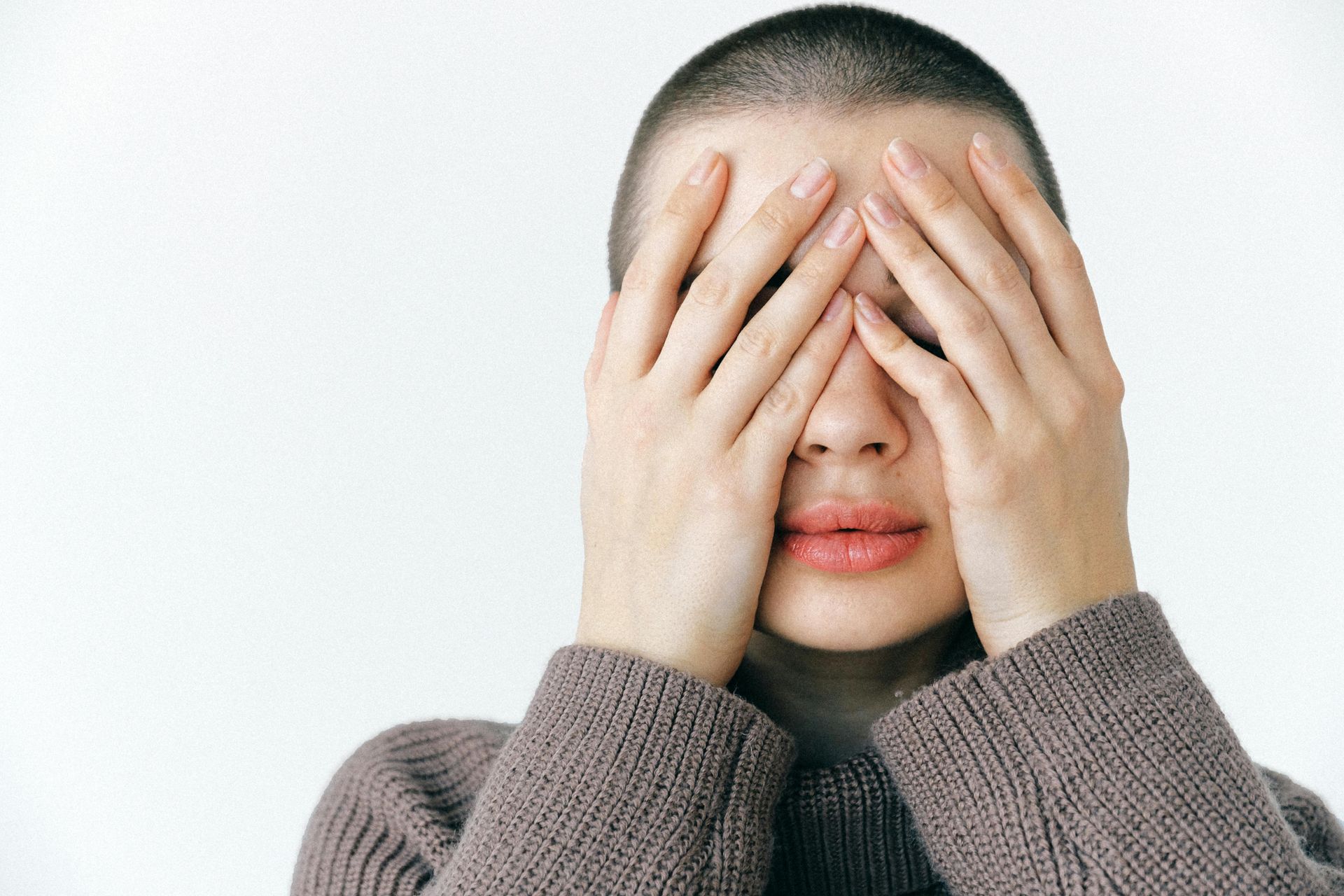 A person stands with their hands covering their eyes and face, as if afraid.