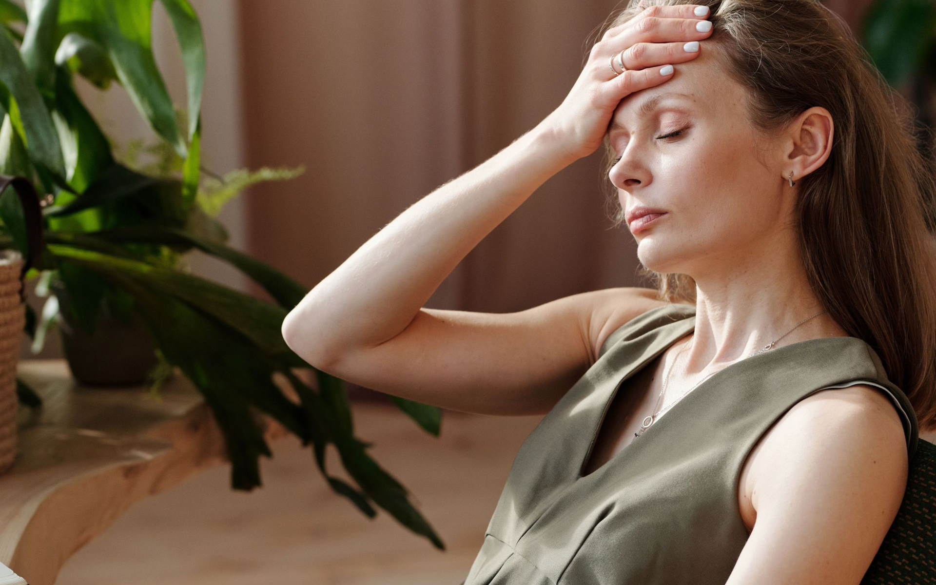 A woman press her hand to her forehead as if she is overwhelmed, overheated, or has a headache.