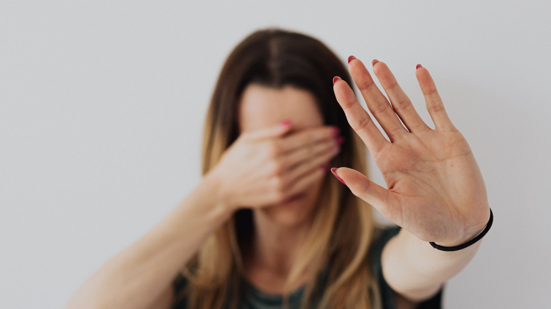A woman covers her eyes with one hand and holds up the other hand, palm outward, in a 'stop' gesture. A woman covers her eyes with one hand and holds up the other hand, palm outward, in a 'stop' gesture.