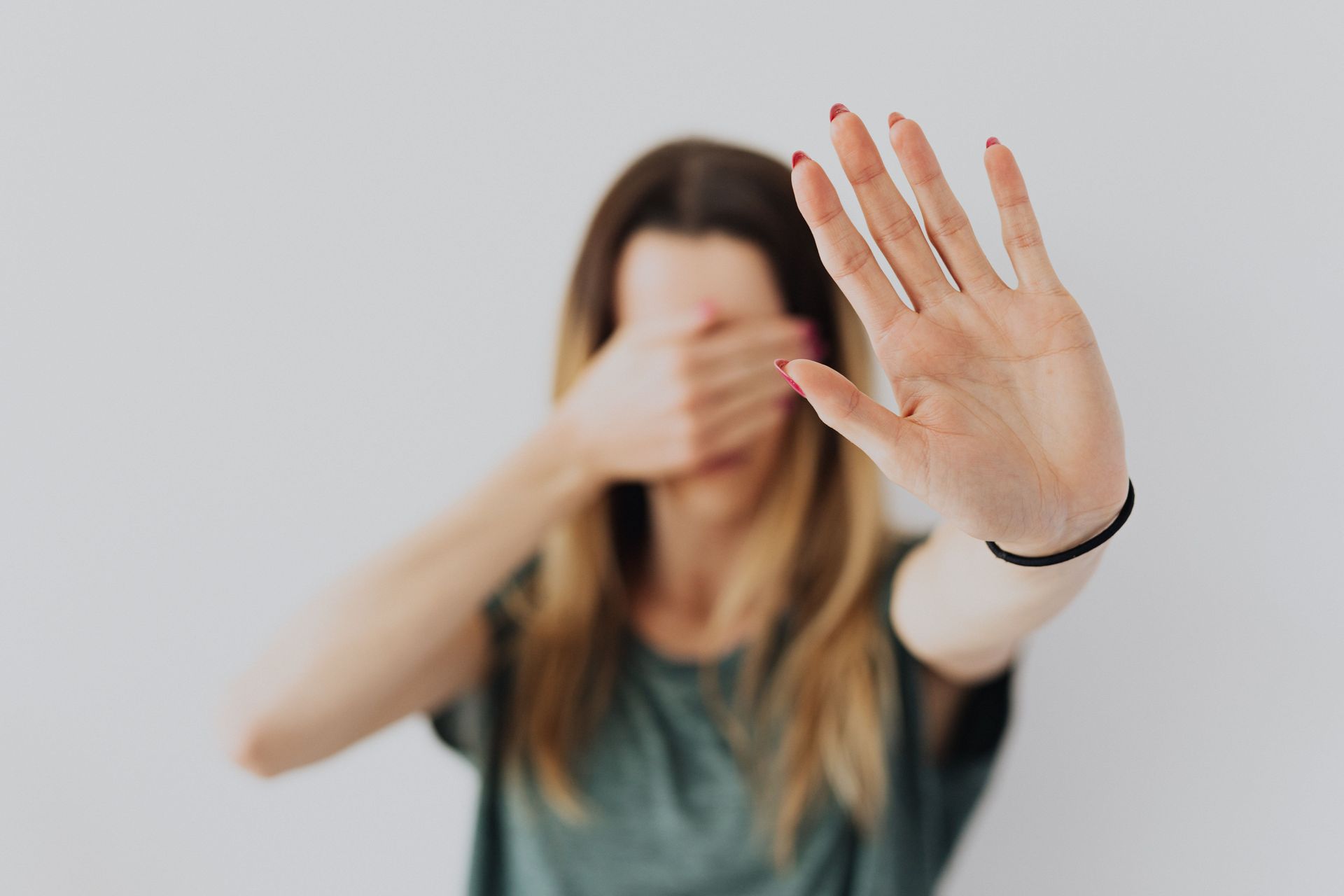 A woman covers her eyes with one hand and holds up the other hand, palm outward, in a 'stop' gesture