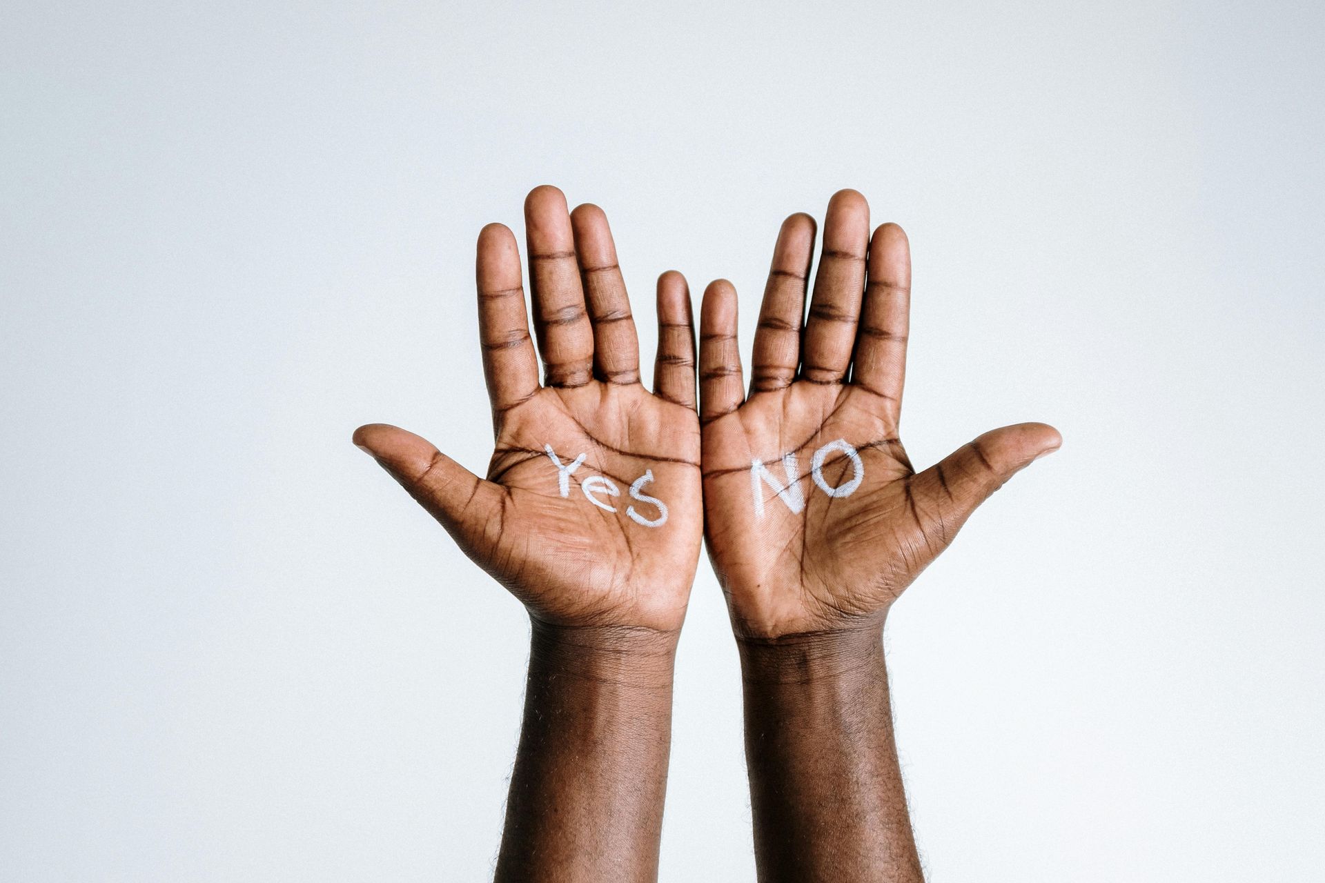 Two hands raised, palms facing upward, with 'yes' written on one hand and 'no' written on the other.