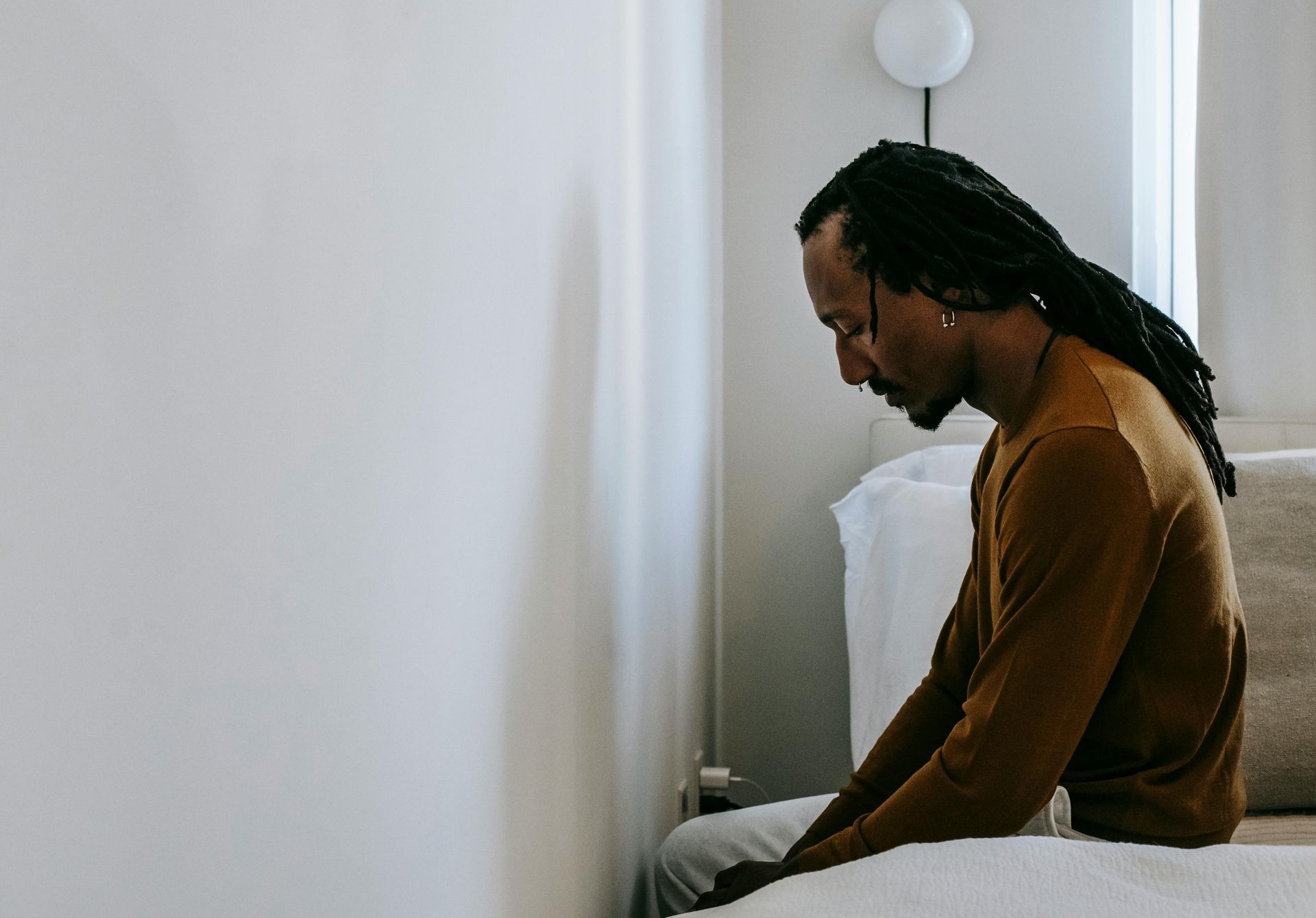 A person sits at the edge of a bed, slumped forward, seeming despondent. 