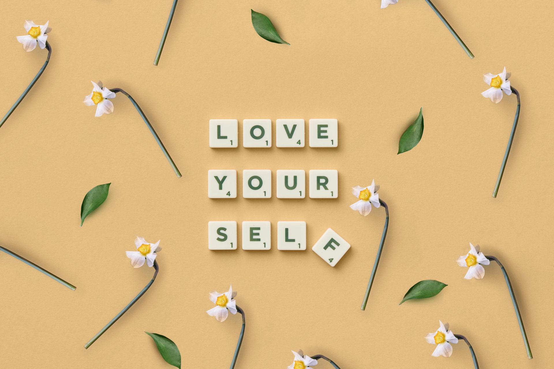 Letter tiles spell out 'love yourself' and are surrounded by daisies. 