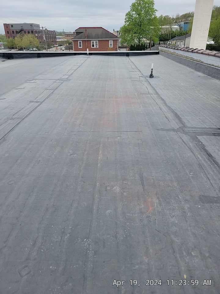 Flat rooftop with gray membrane, skylights, and distant buildings under an overcast sky