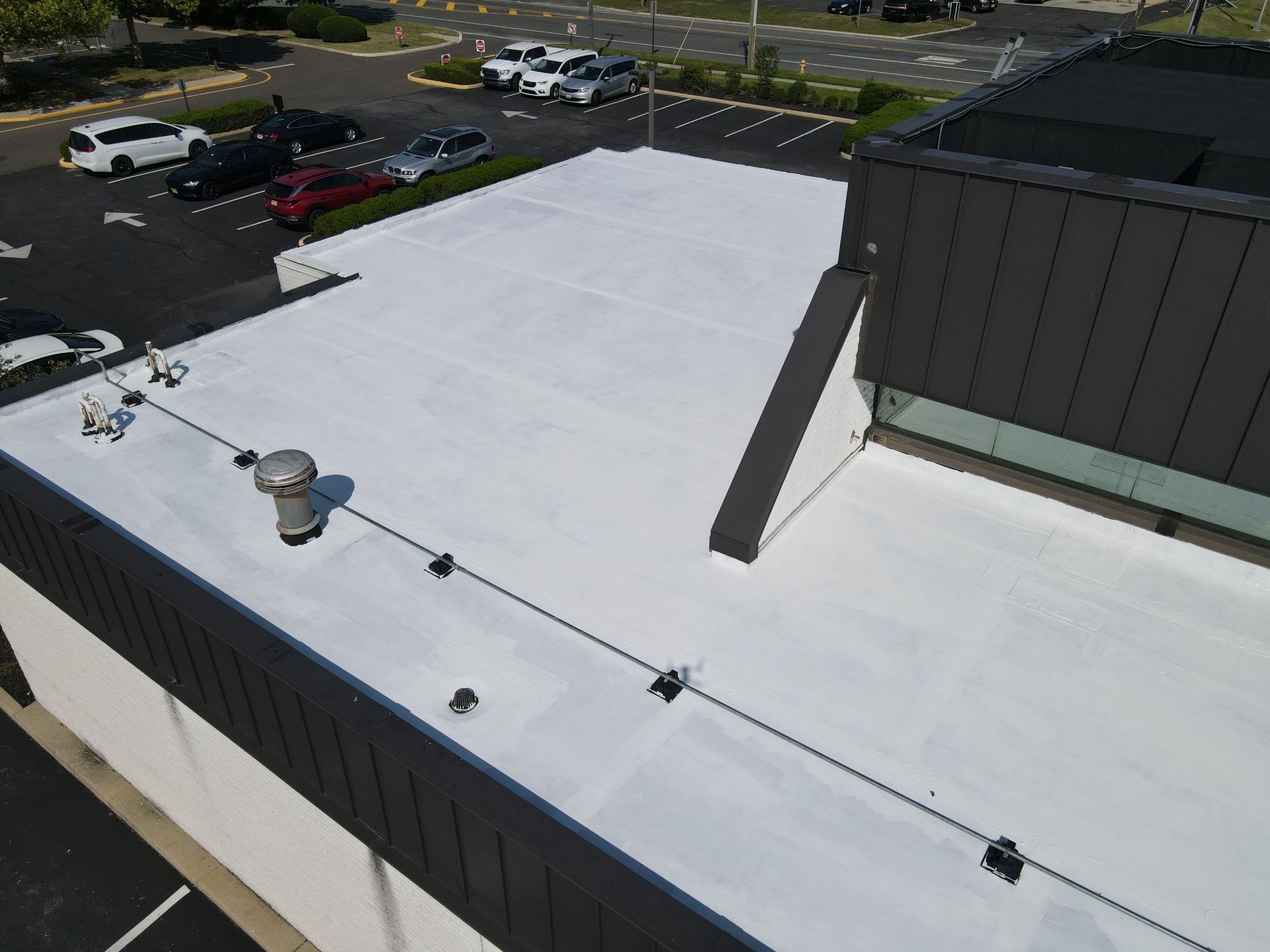 Flat white rooftop with HVAC units and vents beside a parking lot.