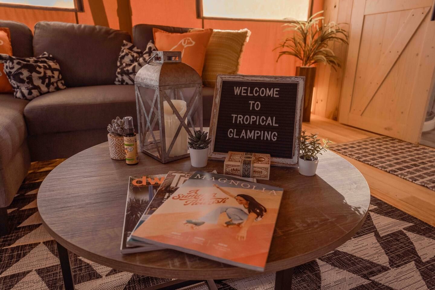 A living room with a couch , table , magazines and a sign that says `` welcome to tropical glamping ''.