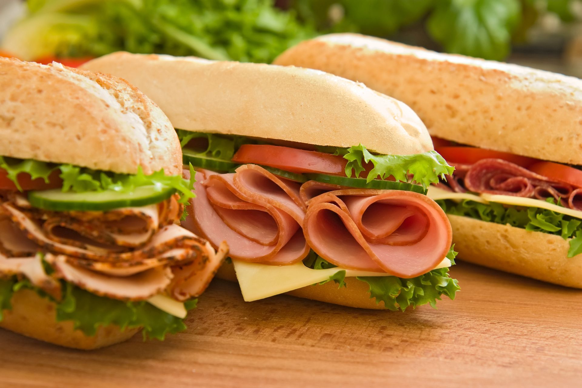 Assorted deli sandwiches on a wooden board with lettuce, cheese, and sliced meat