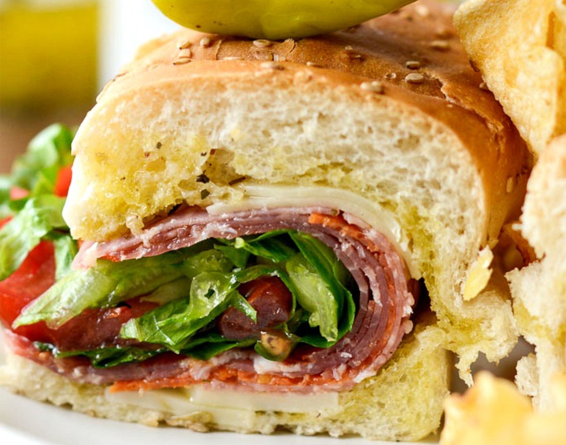 Close-up of a sliced deli sandwich with rolled salami, lettuce, and tomato on crusty bread