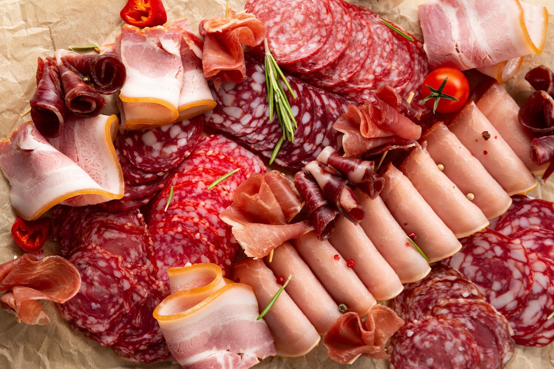 Assorted sliced cured meats and salami arranged on a platter with cherry tomatoes and rosemary