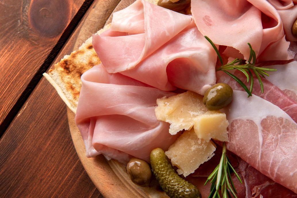 Charcuterie board with sliced cured meats, cheese, pickles, and rosemary on wood