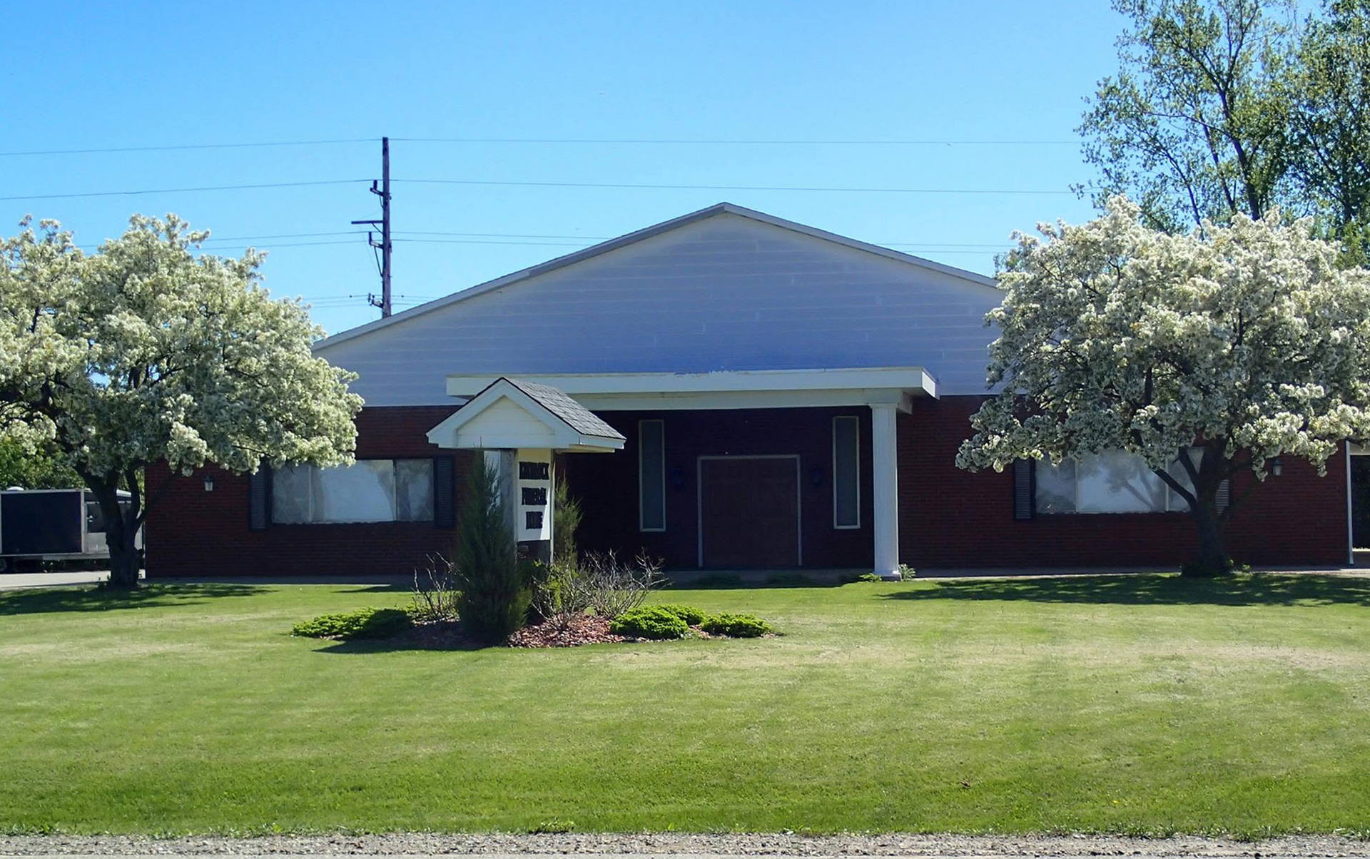 Single-story brick building with white columns, large lawn, and trees in front