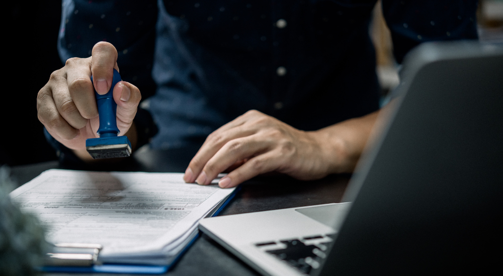 A man is stamping a document in front of a laptop.