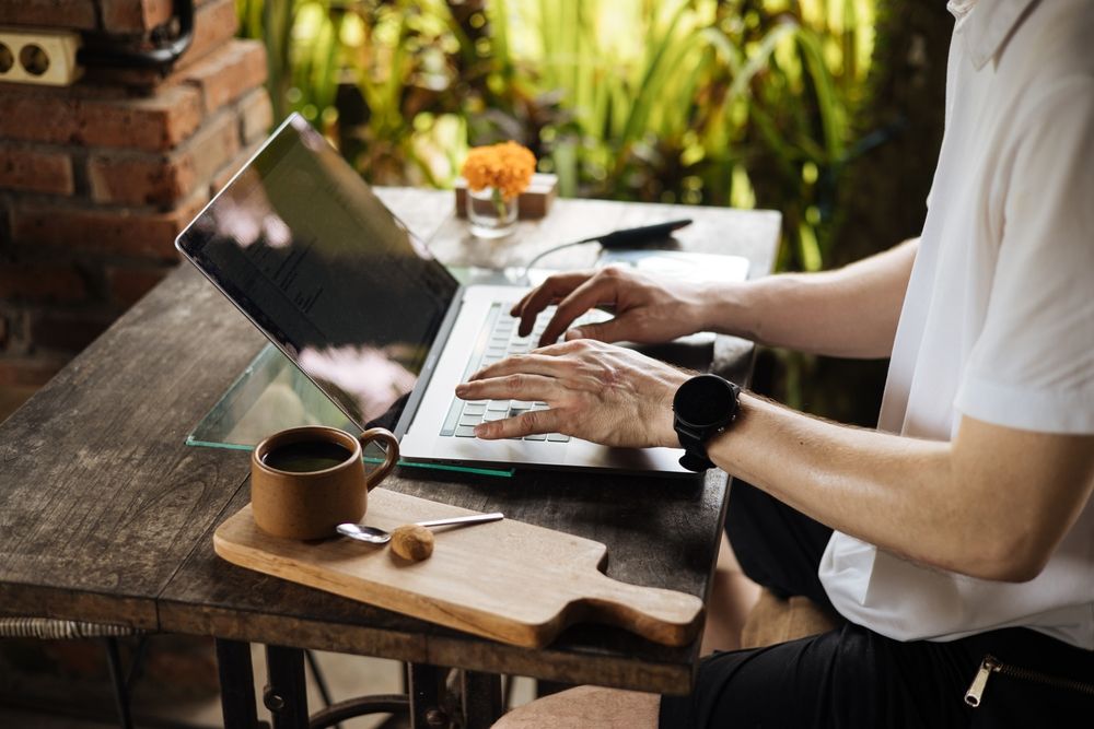 Um homem está sentado a uma mesa digitando em um laptop.