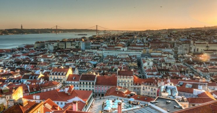 Uma vista aérea de uma cidade ao pôr do sol com uma ponte ao fundo.