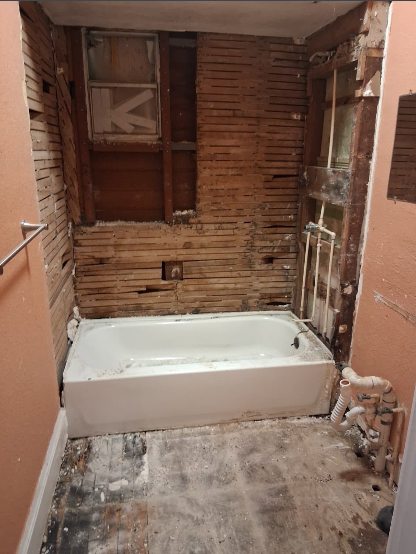 Partially renovated bathroom with exposed studs, a white tub, and unfinished floor and walls.
