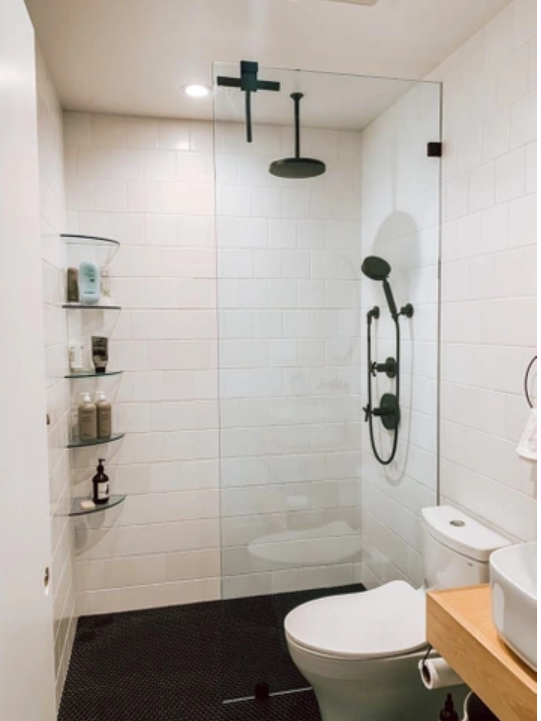 Modern white bathroom with glass shower, black fixtures, toilet, and wooden vanity