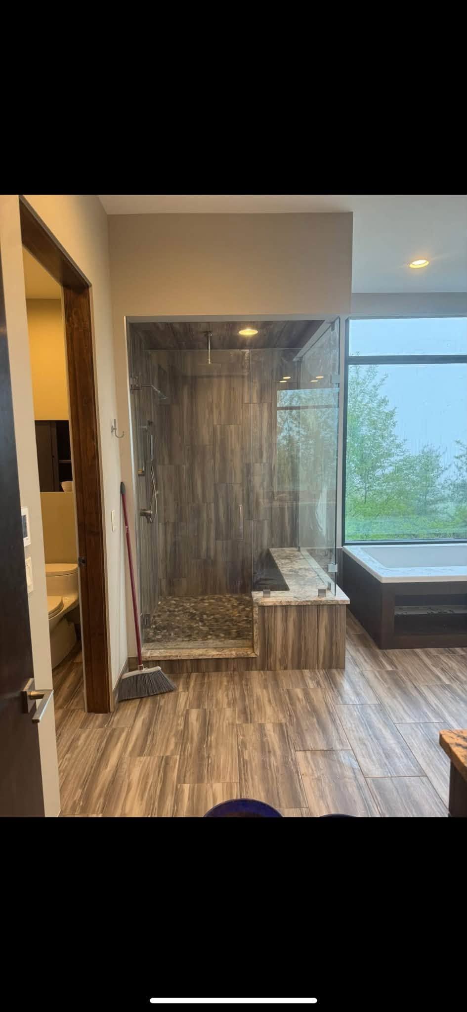 Modern bathroom with glass shower, wood accent wall, and vanity by a window.