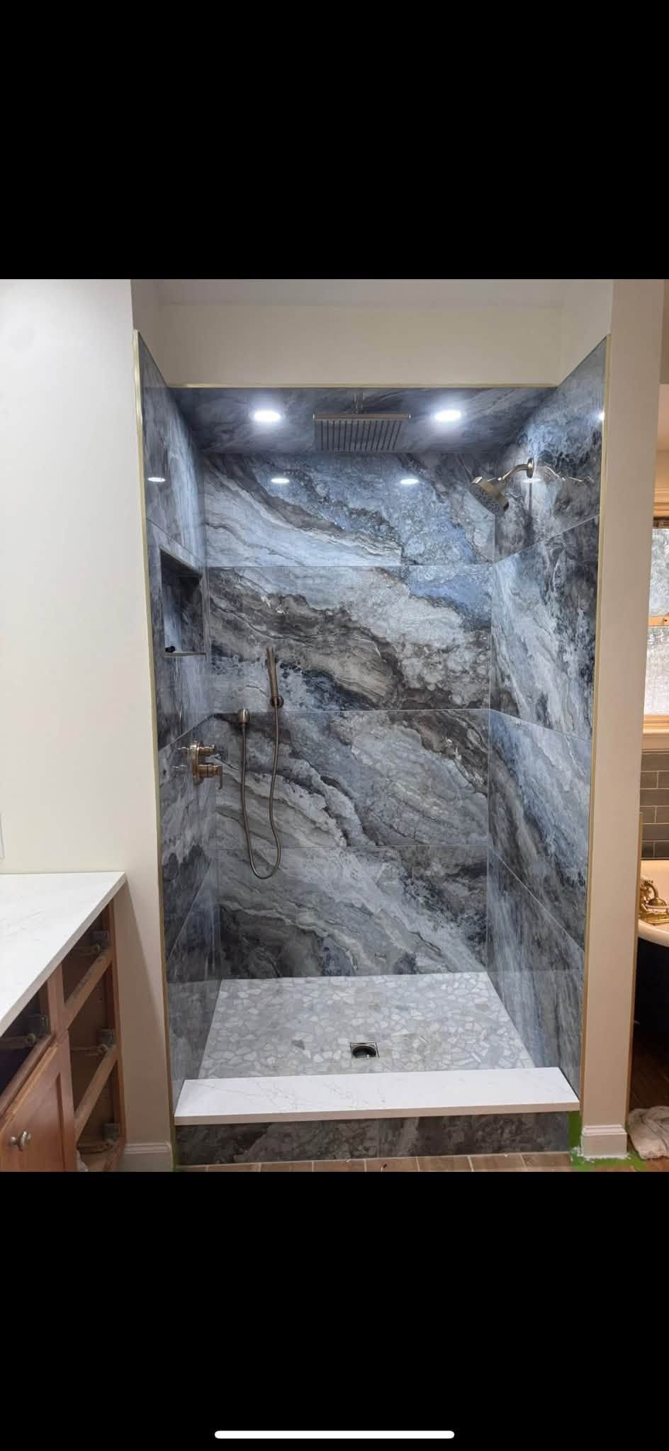 Modern shower alcove with gray marble-pattern tile, recessed lights, and white bench and floor base