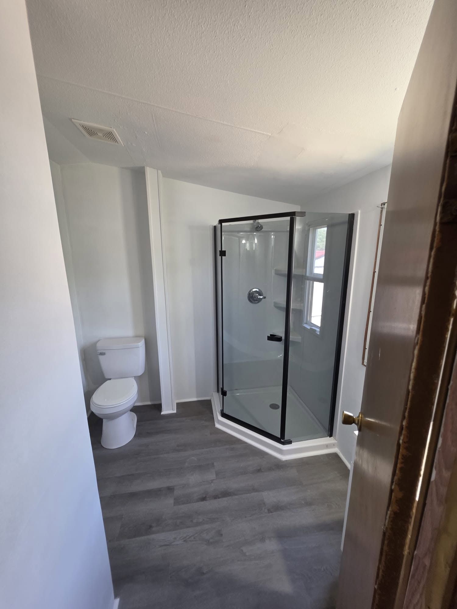 Small bathroom with toilet, glass shower, and gray wood-look floor.
