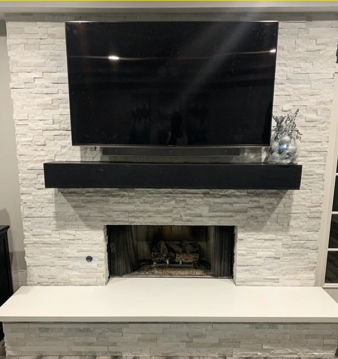 Modern living room fireplace with white stone surround, black mantel, wall-mounted TV, and bench hearth